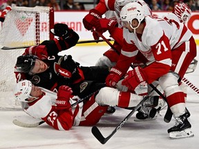Red Wings forward Lucas Raymond (23) and Senators captain Brady Tkachuk (7) fall to the ice as Detroit captain Dylan Larkin (71) looks on during the first period of Saturday's contest.