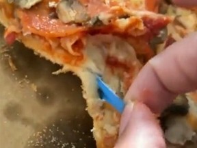 Screengrab of fingers pulling out part of blue glove from under toppings of pizza.