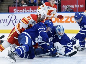 Flames centre Nazem Kadri (91) falls on Maple Leafs defenceman Jake McCabe (22) as goaltender Joseph Woll (60) tries to keep the puck out of the net during first period NHL action in Toronto, Friday, Nov. 10, 2023.