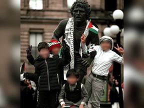 Children holding Palestinian flags climb on the Terry Fox statue statue, which was draped with a pro-Palestinian scarf, to pose for a photo in Ottawa.