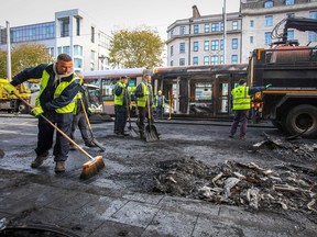 Workers clear the remains of a burnt out bus from a road as a fire-damaged tram stands in the background, on O'Connell Street in Dublin on November 24, 2023.