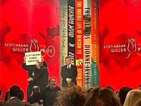 A protestor holding a sign saying "SCOTIABANK FUNDS GENOCIDE" is escorted off the stage during the Scotiabank Giller Prize in Toronto, on Monday, Nov. 13, 2023. (AP Photo/Rob Gillies)