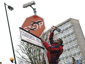 A person removes a piece of art work by Banksy, which shows what looks like three drones on a traffic stop sign, which was unveiled at the intersection of Southampton Way and Commercial Way in Peckham, south east London, Friday Dec. 22, 2023.