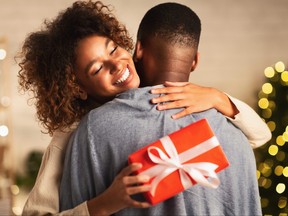Thankful afro woman with christmas gift hugging husband at home