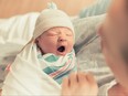 Yawning newborn in swaddle being held by mother.