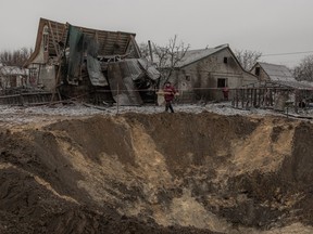 Communal workers walk next to a crater and destroyed houses following a Russian shelling in Kyiv, on December 11, 2023.