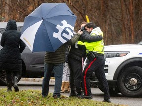 Ottawa Police Service officer, right, hugs a person at a parking lot in Ottawa's Manotick region on Thursday, Dec. 28, 2023. A teenager is dead and another is still missing after four youths fell through the ice on the Rideau River in Ottawa's south end just before midnight on Wednesday.