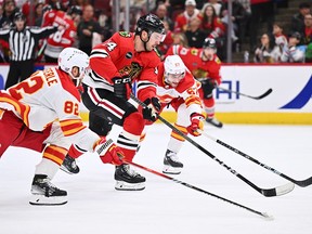 Boris Katchouk #14 of the Chicago Blackhawks carries the puck into the offensive zone while being defended by Jordan Oesterle #82 and Nick Desimone #57 of the Calgary Flames in the second period on January 7, 2024 at United Center in Chicago, Illinois.