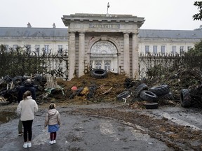 People watch slurry, manure and tyres dumped by farmers at the entrance of the local state administration building, in Agen, southwestern France, Saturday, Jan. 27, 2024. French farmers have vowed to continue protesting and are maintaining traffic barricades on some of the country's major roads. The government announced a series of measures Friday but the farmers say these do not fully address their demands.