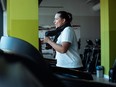 Side view of woman running on treadmill at gym with towel around her neck