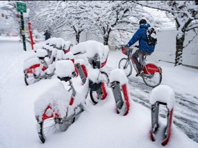 A person cycles past a snow covered bike stand during a snowstorm in Vancouver Wednesday, Jan. 17, 2024.
