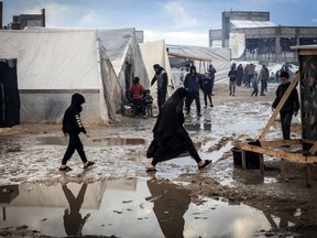 Palestinians make their way on a muddy path past tents at a makeshift camp housing displaced Palestinians, in Rafah in the southern Gaza Strip, on January 2, 2024.