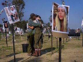 Israeli soldiers embrace next to photos of people killed and taken captive by Hamas militants during their violent rampage through the Nova music festival in southern Israel, which are displayed at the site of the event, to commemorate the October 7, massacre, near kibbutz Re'im, on Friday, Dec. 1, 2023.