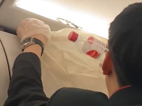 A male AirAsia flight attendant tries to bag a snake that appeared above an overhead bin.