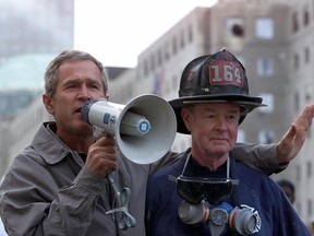 US President George W. Bush (L), standing next to retired firefighter Bob Beckwith, 69, speaks to volunteers and firemen as he surveys the damage at the site of the World Trade Center in this 14 September 2001 file photo in New York. The New York City Fire Department announced on February 5, 2024, the death of retired firefighter Robert Beckwith, who rushed to the scene of the September 11, 2001 attacks and became famous for standing next to President George W. Bush on the ruins of the World Trade Center.