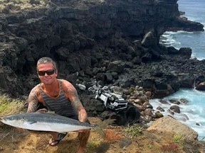 Mike Moody, as shown in this handout image, was fishing off the Big Island of Hawaii early Sunday when a Canadian tourist drove his rented Jeep off a cliff. Moody poses with his catch of the day and the Canadian man's mangled Jeep in the background in this undated photo