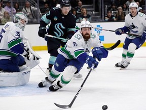 Vancouver Canucks defenceman Filip Hronek reaches for a blocked shot by goaltender Thatcher Demko with Seattle Kraken centre Yanni Gourde skating behind during the game Thursday in Seattle.