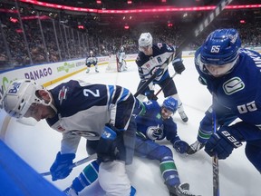 Winnipeg Jets' Dylan DeMelo (2) vies for the puck against Vancouver Canucks' Ilya Mikheyev (65) and Teddy Blueger (53) as Winnipeg's Mark Scheifele, back centre, watches during the first period of an NHL hockey game in Vancouver, on Saturday, Feb. 17, 2024.
