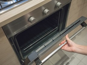 A woman opens the black and silver door of an oven.