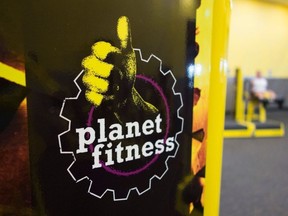 A Planet Fitness sign is seen as a woman does leg lifts in background.