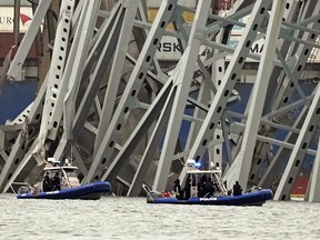 Police boats work around a cargo ship that is stuck under part of the structure of the Francis Scott Key Bridge after the ship hit the bridge Wednesday, March 27, 2024, in Baltimore.