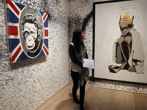 A woman stands in front of two pieces of work entitled "Monkey Queen" and "Burger King Kid" during a press preview of the first unauthorized retrospective of works by U.K. artist Banksy, in London, England, June 6, 2014.