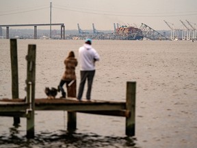 People look out toward the Francis Scott Key Bridge following its collapse after the Singapore-flagged Dali container ship collided with it along the Patapsco River on March 26, 2024 in Baltimore, Maryland.