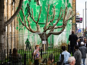 Members of the public look at a mural by Banksy following its defacement with white paint, on March 20, 2024 in the Finsbury Park area of London, England.