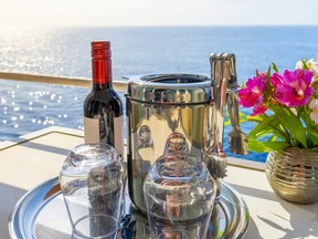 A bottle of red wine, ice bucket and stemless glasses on the balcony deck of a cruise ship cabin at sea on a summer day.