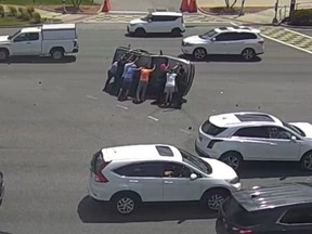 Screenshot of eight people trying to flip car on its side back onto its wheels.