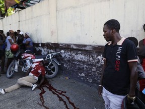 Motorcyclists navigate around a charred body lying in the road as pedestrians walk past, in the Petion-Ville neighborhood of Port-au-Prince, Haiti, Wednesday, March 20, 2024.