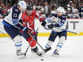 Washington Capitals right wing Nicolas Aube-Kubel (96) tries to maneuver the puck between Winnipeg Jets right wing Tyler Toffoli (73) and defenceman Josh Morrissey (44) in the second period of an NHL hockey game, Sunday, March 24, 2024, in Washington.