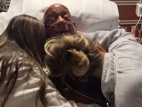 Screenshot of Mark Coleman in hospital bed hugging daughters.