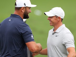 Jon Rahm and Rory McIlroy shake hands in the practice area at the 2024 Masters Tournament.