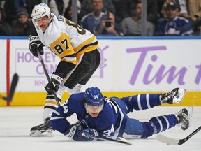 Sidney Crosby 87 of the Pittsburgh Penguins knocks Auston Matthews #34 of the Toronto Maple Leafs down as he is passing the puck during an NHL game at Scotiabank Arena on November 20, 2021 in Toronto, Ontario, Canada.
