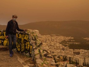 A man wearing a mask walks at the Lycabettus hill as the city of Athens is seen at the background, on Tuesday, April 23, 2024.