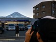 This photo taken on January 1, 2024 shows a tourist posing in front of a convenience store with Mount Fuji in the background, in the town of Fujikawaguchiko, Yamanashi prefecture. A huge black barrier to block Mount Fuji from view will be installed in a popular photo spot by Japanese authorities exasperated by crowds of badly behaved foreign tourists, it was reported on April 26, 2024.