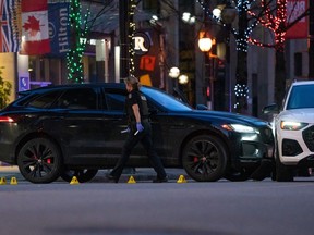 A Vancouver police officer walks past a black SUV surrounded in evidence cones after shutting down part of Robson Street for a shooting incident in Vancouver, Saturday, March. 30, 2024.