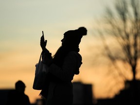 A person silhouetted against the evening sky takes a photo with a smartphone in Philadelphia, Thursday, Dec. 12, 2019.