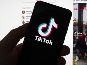 The TikTok logo is seen on a mobile phone in front of a computer screen which displays the TikTok home screen, March 18, 2023, in Boston.