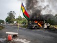 A Kanak flag stands next to a burning vehicle at a roadblock at La Tamoa, in the commune of Paita in France's Pacific territory of New Caledonia on Sunday, May 19, 2024. French forces smashed through about 60 road blocks to clear the way from conflict-stricken New Caledonia's capital to the airport but have still not reopened the route, a top government official said.