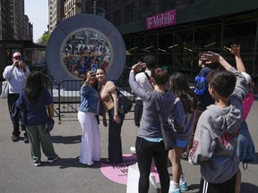 People wave and take pictures while looking at a livestreamed view in Dublin, Ireland, as part of an art installation on the street in New York, Tuesday, May 14, 2024.