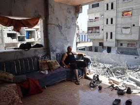 TOPSHOT - A Palestinian man sits on a sofa with the remains of exploded ordnance at his feet in a partially destroyed apartment, looking down at the demolished building where Israeli hostages were purportedly being held and rescued during an Israeli military operation a week ago, in the Nuseirat refugee camp, in the central Gaza Strip on June 15, 2024, amid the ongoing conflict between Israel and the Palestinian Hamas militant group. Israel announced its forces rescued four hostages on June 8, from the Nuseirat refugee camp in an operation which the Hamas-run government media office said left 210 Palestinians dead and hundreds wounded. The Israeli military said the four, who were in "good medical condition", had been kidnapped from the Nova music festival during Hamas's October 7 attack that sparked war, now in its ninth month. (Photo by Eyad BABA / AFP) (Photo by EYAD BABA/AFP via Getty Images)