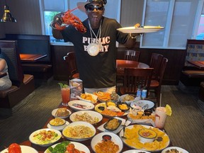 Rapper Flavor Flav holding lobster and plate in front of table holding Red Lobster menu items.