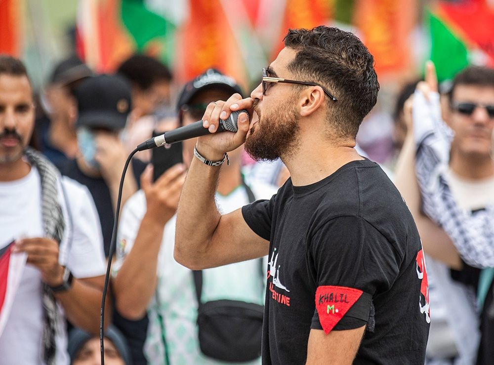 An organizer of the Sunday, Aug. 11 anti-Israel protest in Ottawa speaks to the crowd, wearing an inverted red triangle on his shirt. The triangle, used by Hamas to mark targets and intimidate opponents, has become a controversial symbol in Canada.