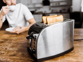 cropped shot of young man drinking coffee at home with toaster on foreground