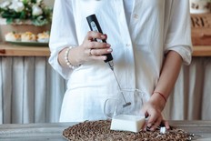 Mixing milk in glass pot by frother close up. Woman making foamy milk with handheld mixer. Housewife female iusing mixer whips cooking food in kitchen at home
