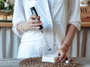 Mixing milk in glass pot by frother close up. Woman making foamy milk with handheld mixer. Housewife female iusing mixer whips cooking food in kitchen at home