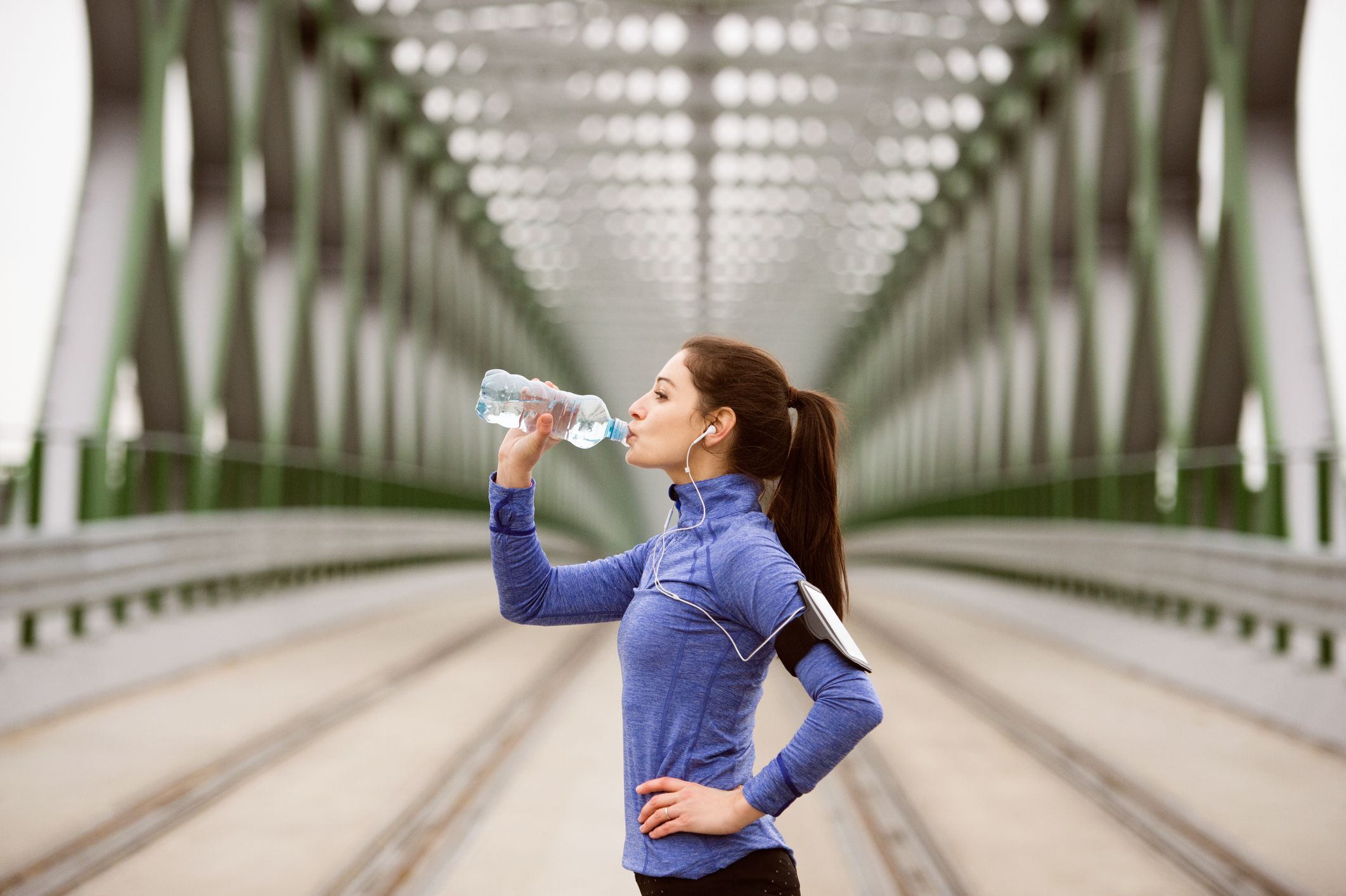 Young runner resting, drinking water on green steel bridge