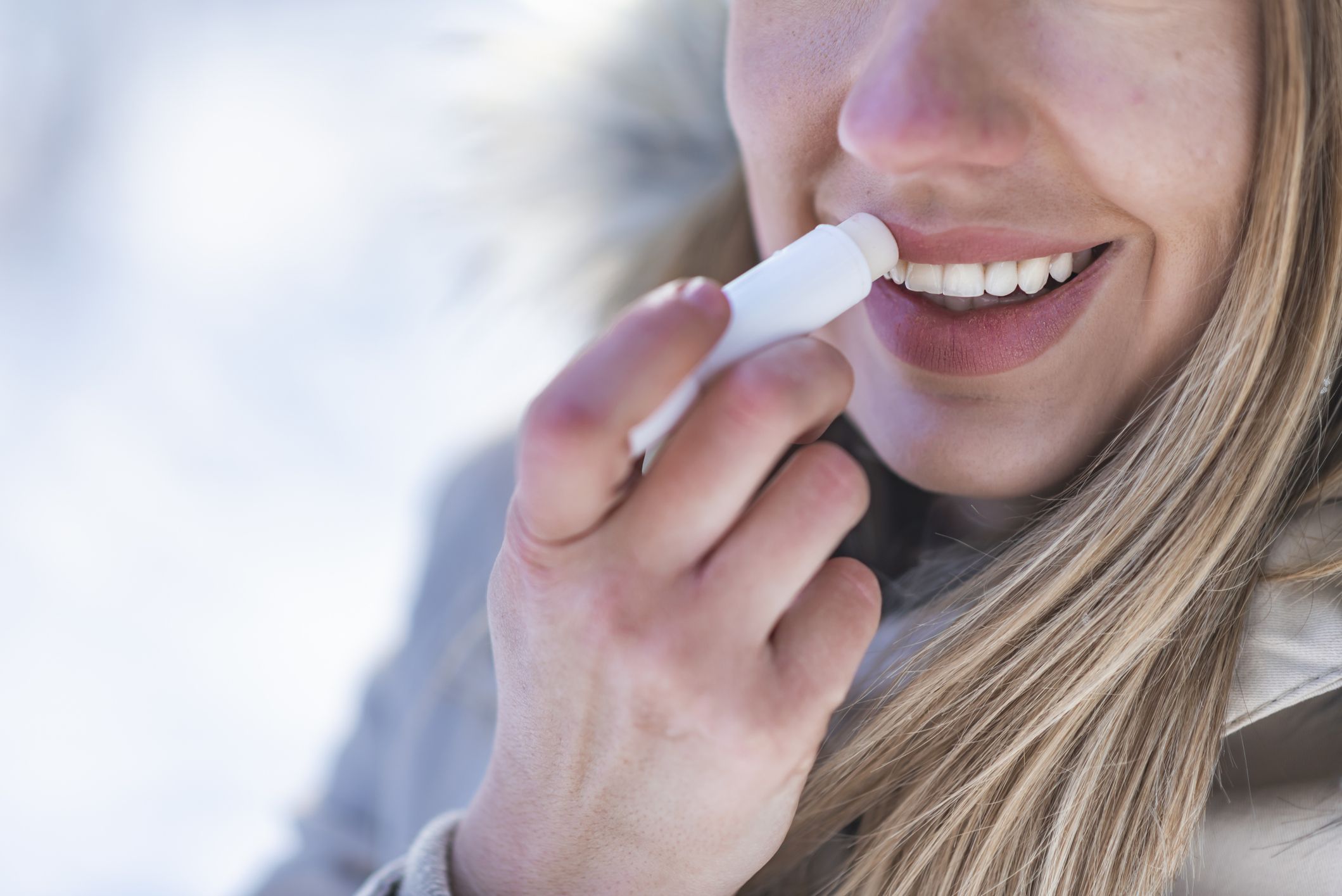 Portrait of young female applying lip balm in winter. Portrait of a beautiful woman in snow with application of the protective cream to the lips